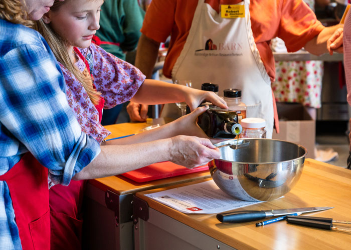Youth pouring olive oil with adult help in Kitchen class